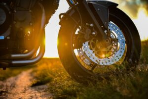 Detalle de la rueda delantera y freno de una motocicleta al atardecer; imagen referencial